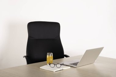 Boş siyah sandalye boş bir dizüstü bilgisayar, defter, okuma gözlüğü ve bir bardak meyve suyu. Boşluk yok. Reklam için alanı kopyala.