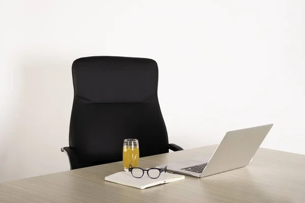 Empty black chair at a desk with a open laptop, notebook, reading glasses and glass of juice. Negative space. Copy space area for advertising.