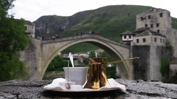 Traditional Turkish coffee and a view of Mostar Old bridge and river Neretva. Bosnian coffee in a cezve with a turkish delight, Mostar, Bosnia And Herzegovina.