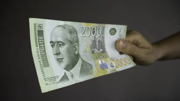 The hand gives money - Serbian 2000 dinar currency banknote. Serbia money RSD dinar cash. Dinars with a portrait of a climate scientist Milutin Milankovic.