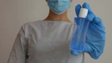 Cerrahi maskeli bir kadın iki elinde de plastik alkol jeli tutuyor..