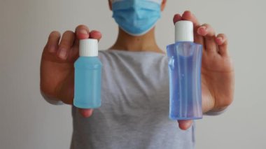 Cerrahi maskeli bir kadın plastik el dezenfektanı şişelerini çeker..