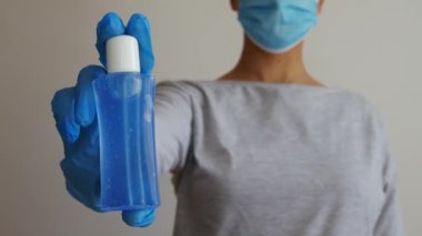 Tıbbi maskeli ve lastik eldivenli bir kadının elindeki alkol jölesi..