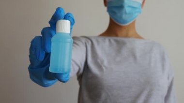 Cerrahi maskeli bir kadın plastik bir el dezenfektanı şişesi tutuyor. Coronavirus konsepti - alkol jeli.