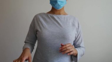 Mavi cerrahi maskeli bir kadın ellerine mavi lastik eldiven takar ve baş parmağını kaldırır..