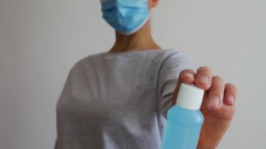 İyi bir ilaç. Tıbbi maskeli bir kadın plastik bir şişe alkol jeli tutuyor ve baş parmağını kaldırıyor.. 