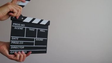 Kadın, ahşap direktörle el ele tutuşup boş siyah film izleyerek gri arka planda klaket oluşturur. Sinematografi üretim konsepti. Uzay reklamını kopyala. Üç farklı pozisyon ve üç alkış..