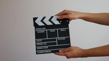 Kadın, ahşap direktörle el ele tutuşup boş siyah film izleyerek gri arka planda klaket oluşturur. Sinematografi üretim konsepti. Uzay reklamını kopyala. Üç farklı pozisyon ve üç alkış..