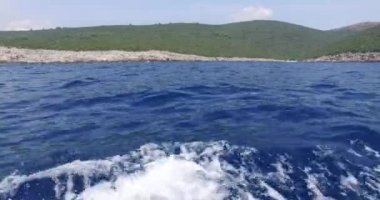Mavi denizde, yeşil bir tepenin yanında.