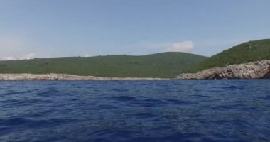 Yeşil bir tepenin yanında mavi denize yelken açmak ve hareket halindeki bir teknenin kenarından sarkan beyaz şamandıra..