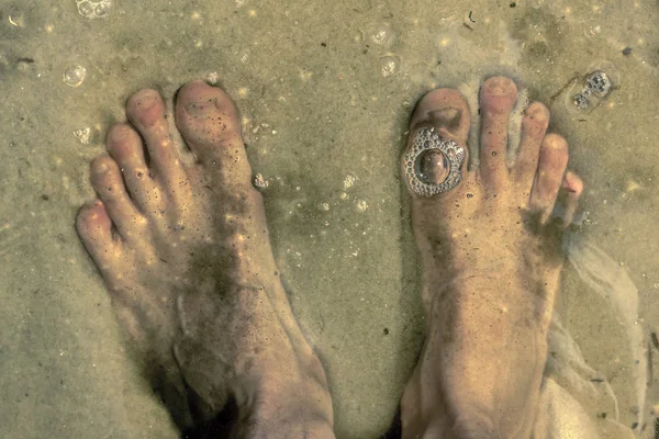 Pies bajo el agua de pie sobre fondo arenoso y burbujas en wat — Foto de Stock