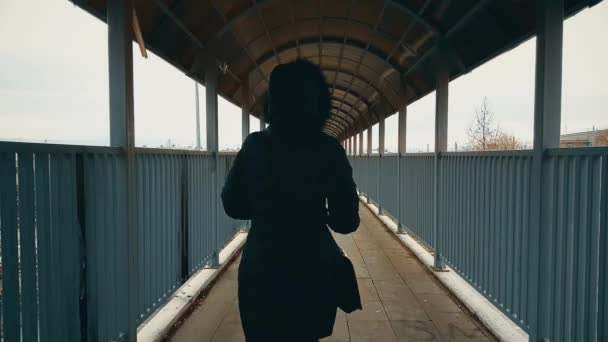 Lopende vrouw met zwarte jas kruising van de voetgangersbrug over de snelweg — Stockvideo