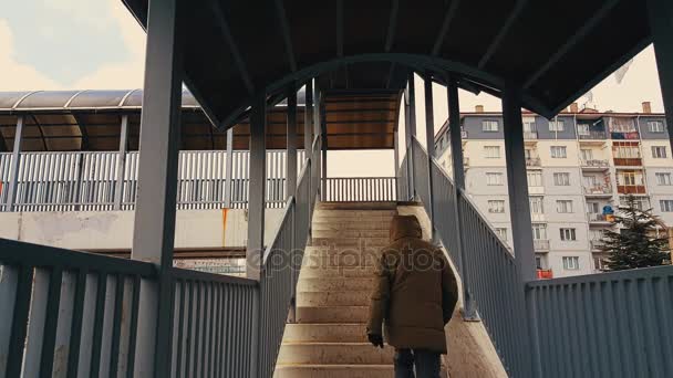En man med beige kappa går uppför trappan av gångbron — Stockvideo