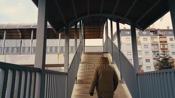 Un homme avec un manteau beige qui monte les escaliers de la passerelle — Video