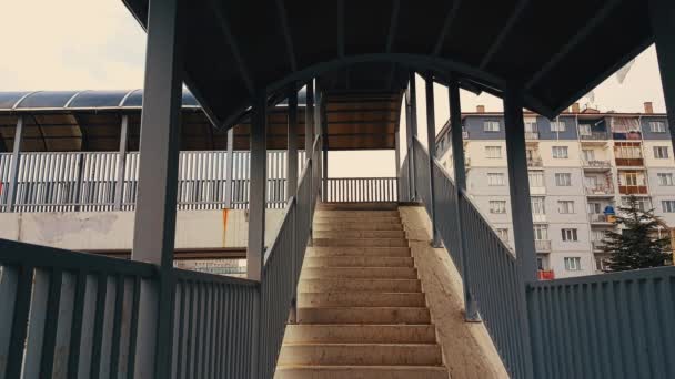Un homme avec un manteau beige et un sac à dos montant les escaliers de la passerelle — Video