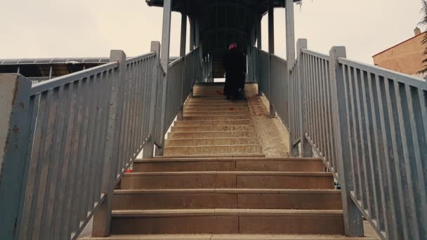 Alte Frau mit schwarzem Mantel und Hijab geht die Treppe der Fußgängerbrücke hinauf — Stockvideo