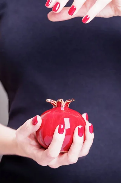 Vacker kvinnlig hand håller keramiska röda granatäpple frukt. Manikyr med rött nagellack. Svart bakgrund — Stockfoto