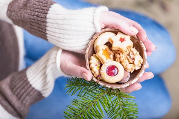 Hermosas manos femeninas sosteniendo un tazón con galletas caseras y rama de árbol de Navidad. Manicura con esmalte de uñas de color beige. Concepto de vacaciones — Foto de Stock