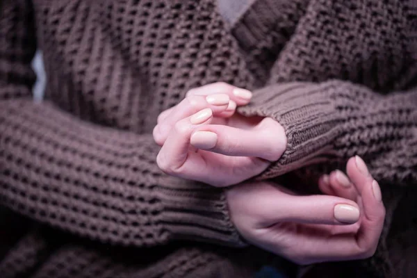 Hermosas manos femeninas en el fondo del suéter de punto marrón. Manicura con esmalte de uñas de color beige, manicura desnuda — Foto de Stock