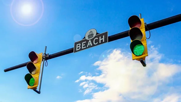 Två trafikljus och gatuskylt Beach. Trafikljus med grönt ljus. Blå himmel med solsken, 16: 9 — Stockfoto