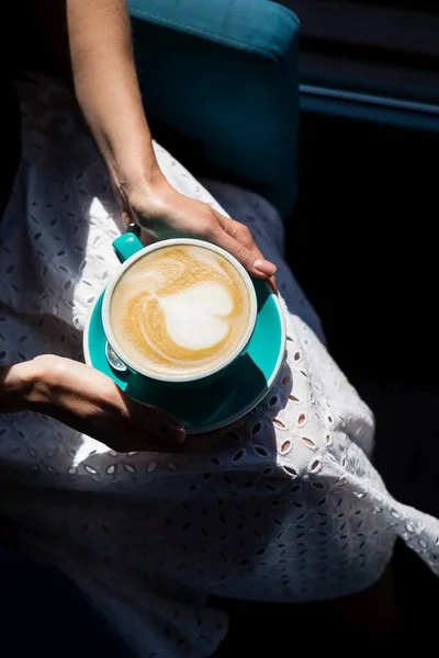 Manos femeninas sosteniendo una taza verde de capuchino café. Manicura con esmalte de uñas desnudo rosa — Foto de Stock