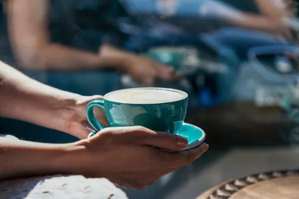 Manos femeninas sosteniendo una taza verde de capuchino café, luz y sombra — Foto de Stock