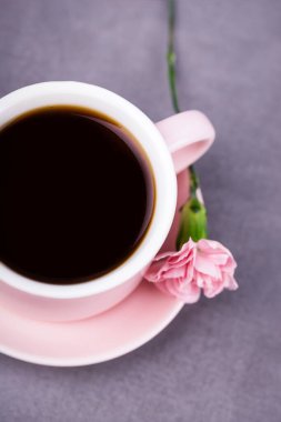Pembe kahve fincanı ve gri beton arka planda pembe karanfil çiçeği.