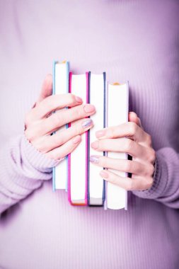 Soluk menekşe arkaplanda dört kitap tutan güzel kadın elleri. Pembe ojeli manikür, parlak tasarım, çıplak manikür, fotokopi alanı