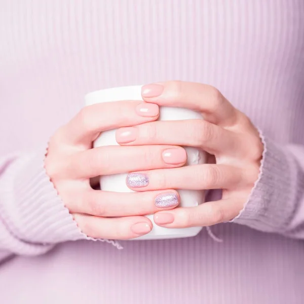 Vackra kvinnliga händer som håller vit kopp på den bleka violetta bakgrunden. Manikyr med rosa nagellack med blank design, naken manikyr. Kopiera utrymme — Stockfoto