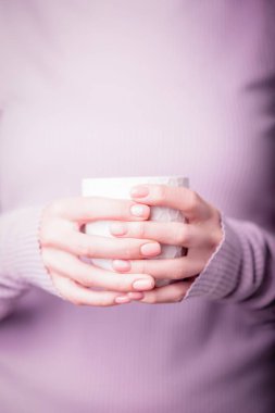Soluk menekşe arka planda beyaz bardağı tutan güzel kadın elleri. Pembe ojeli manikür. Eğreltiotu ve canavar desenli çıplak manikür. Boşluğu kopyala