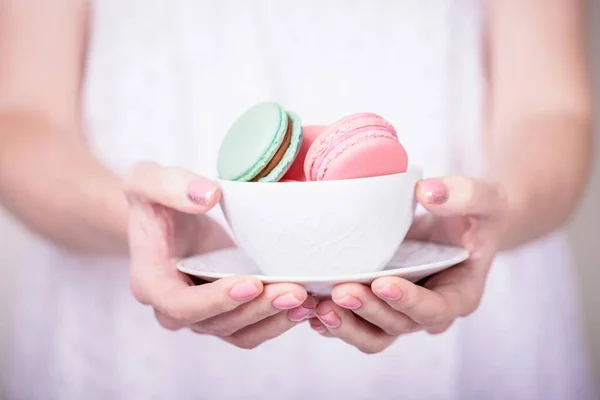 Beautiful female hands holding white cup with pink and mint macaroons. Manicure with pink color nail polish. Manicure with sparkles — Stock Photo, Image