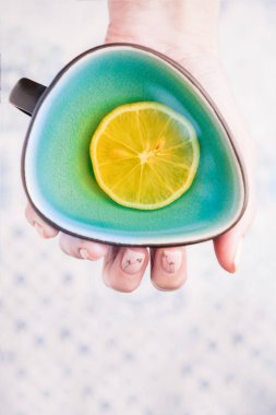 Turkuaz bir bardak limon çayı tutan bir kadın. Üst görünüm, alanı kopyala