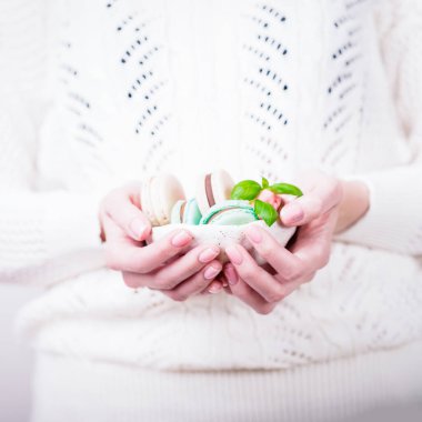 Güzel kadın elleri açık arkaplanda bir kase Fransız renginde badem kurabiyesi tutuyor.