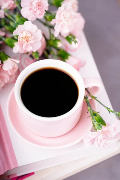Pink cup of black coffee and pastel pink carnation flowers on a light background, vertical