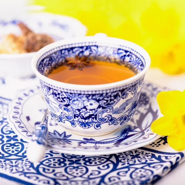 Anasonlu bir fincan çay. Mavi ve beyaz tabaklar ve sarı nergisler