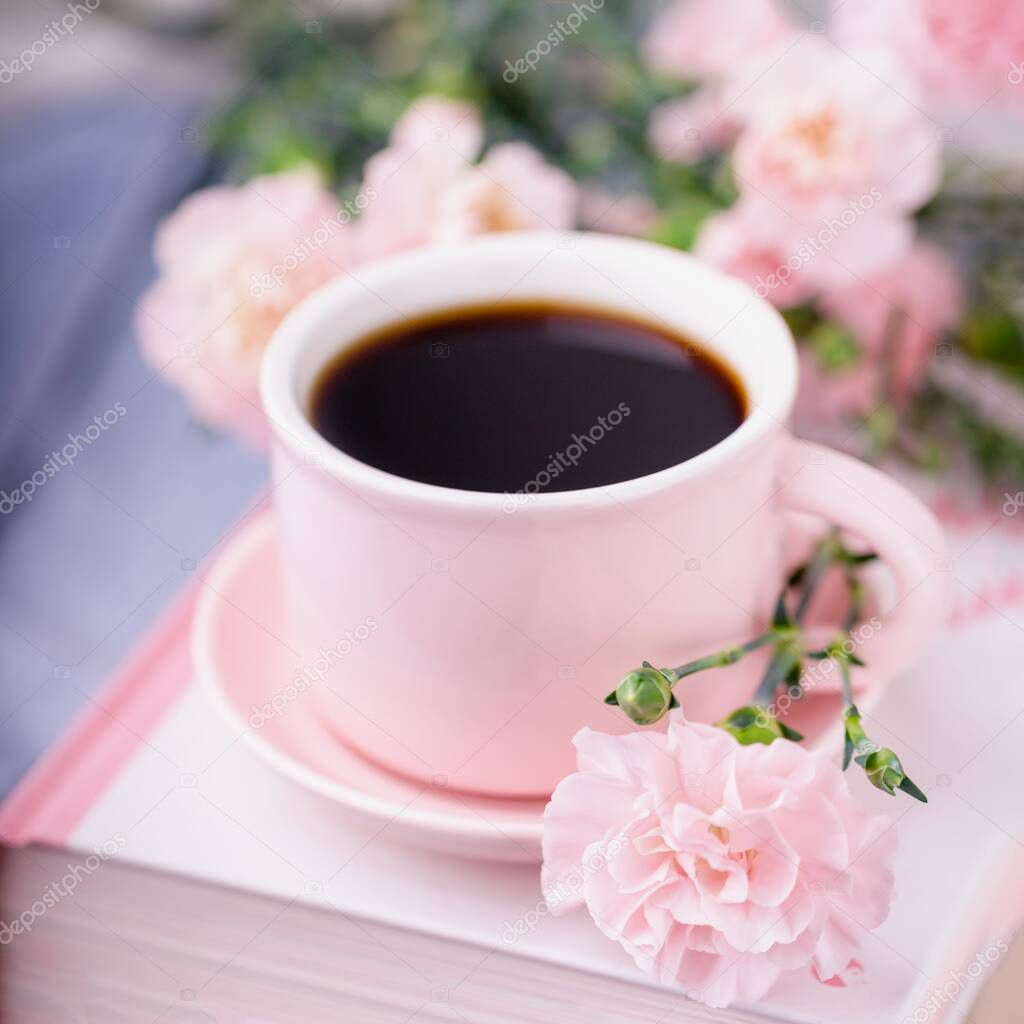 Pink cup of black coffee, books and pastel pink carnation flowers, vertical photo