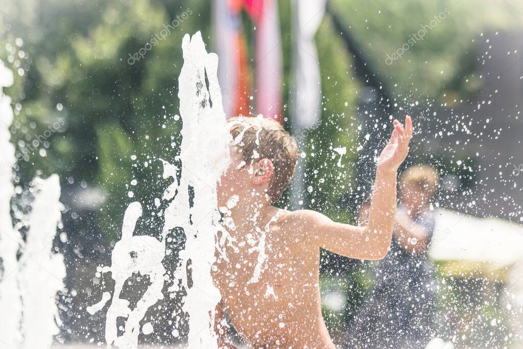 Little boy bathes in a city fountain. Boy having summer fun. Soft focus, defocused photo