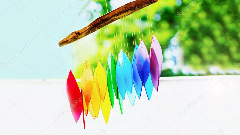 Rainbow glass wind chimes or windchime on nature background. Feng shui symbol, copy space. 16 on 9 panoramic format