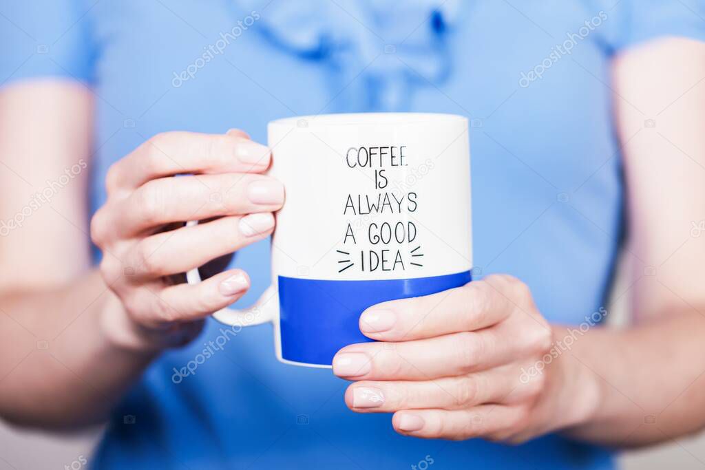 Female hands holding white and blue cup with inscription. Coffee is always a good idea