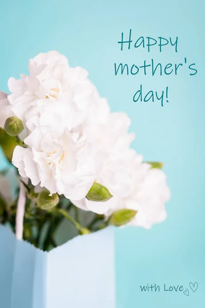 Bonne carte de vœux de la fête des mères. Fleurs oeillet blanc dans un sac cadeau sur le fond d'aigue-marine — Photo