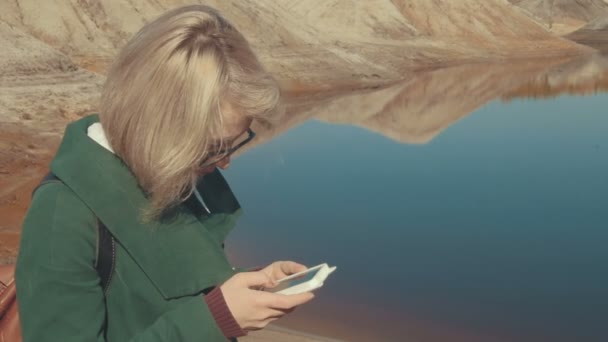 Jonge vrouw in een verlaten landschap staan met haar slimme telefoon in de hand via apps surfen op het internet — Stockvideo