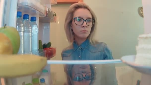 Junge Frau öffnet Kühlschrank und wählt etwas zu essen und nimmt Salat — Stockvideo