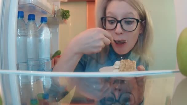 Młoda kobieta otwiera lodówkę, jedzenie ciasto bardzo szybko i pije mleko — Wideo stockowe