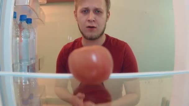 Jeune homme ouvre le réfrigérateur veulent manger, mais ne trouve qu'une tomate et desparately prend et mange — Video