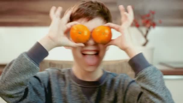 Смешной маленький мальчик держит мандарины перед глазами и веселится — стоковое видео