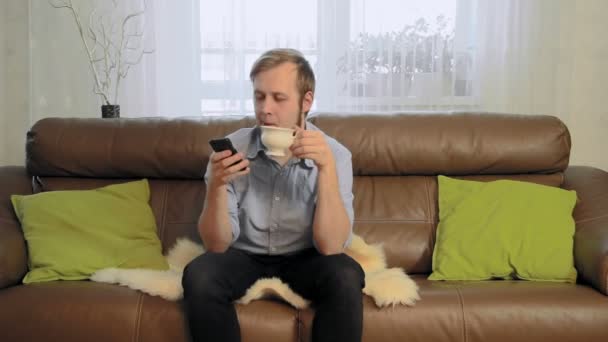 Junger Mann trinkt Tee und benutzt sein Handy — Stockvideo