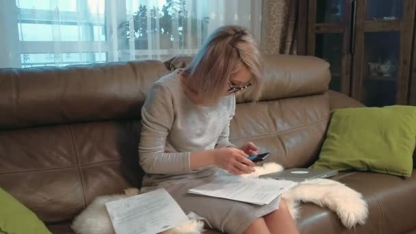 Νεαρή γυναίκα που εργάζεται με χαρτιά και κινητό τηλέφωνο, τον υπολογισμό αριθμών — Αρχείο Βίντεο