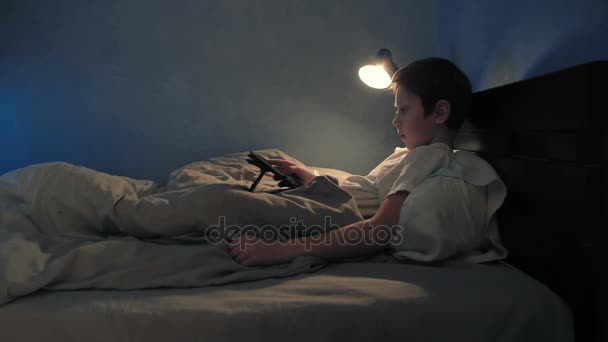 Ragazzo che riposa nel suo letto la sera usando il suo tablet digitale — Video Stock