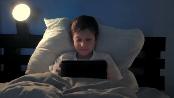 Ανάπαυση στο κρεβάτι του το βράδυ χρησιμοποιώντας ψηφιακό tablet αγόρι — Αρχείο Βίντεο