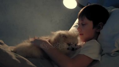 Akşam yatağında dinleniyor ve köpeğiyle oynayan bir çocuk